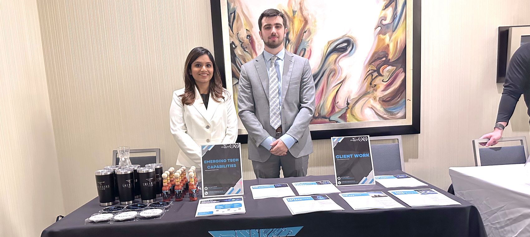 Two Emerging Tech staff at the company's exhibition stand with capability sheets and client work on display